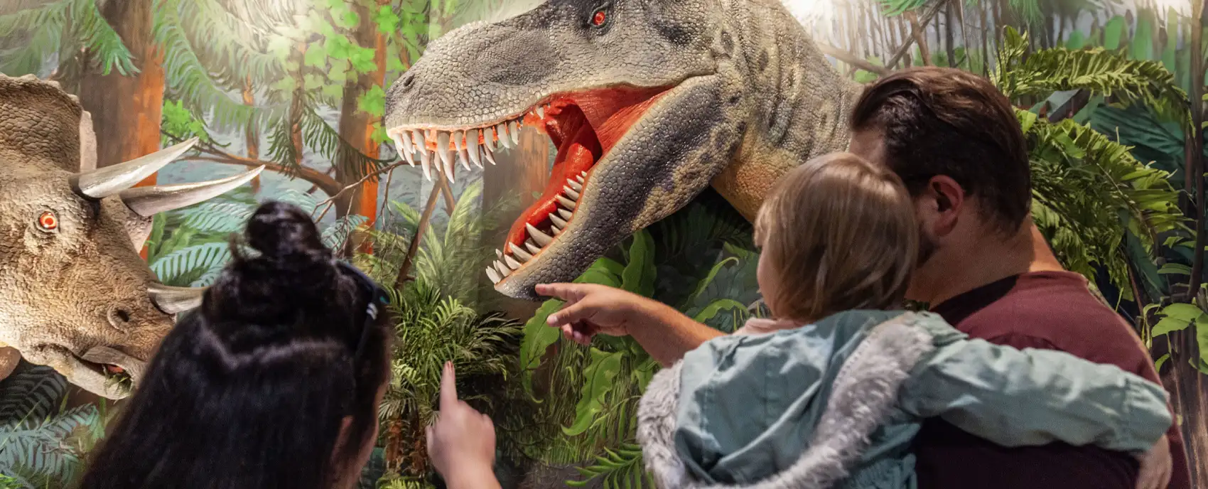 husband and wife holding young child in arms looking at dinosaur
